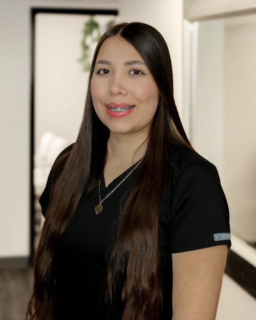 Woman in black shirt smiling at camera in dental office hallway setting.